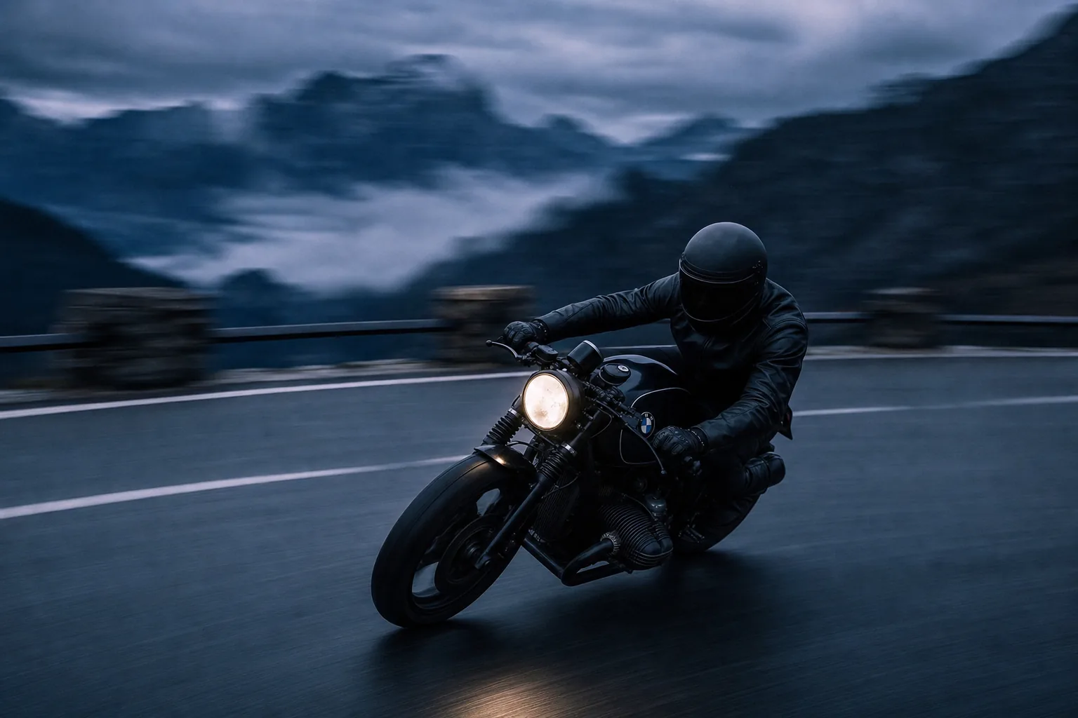 A rider leaning a black BMW cafe racer through a mountain corner at dusk
